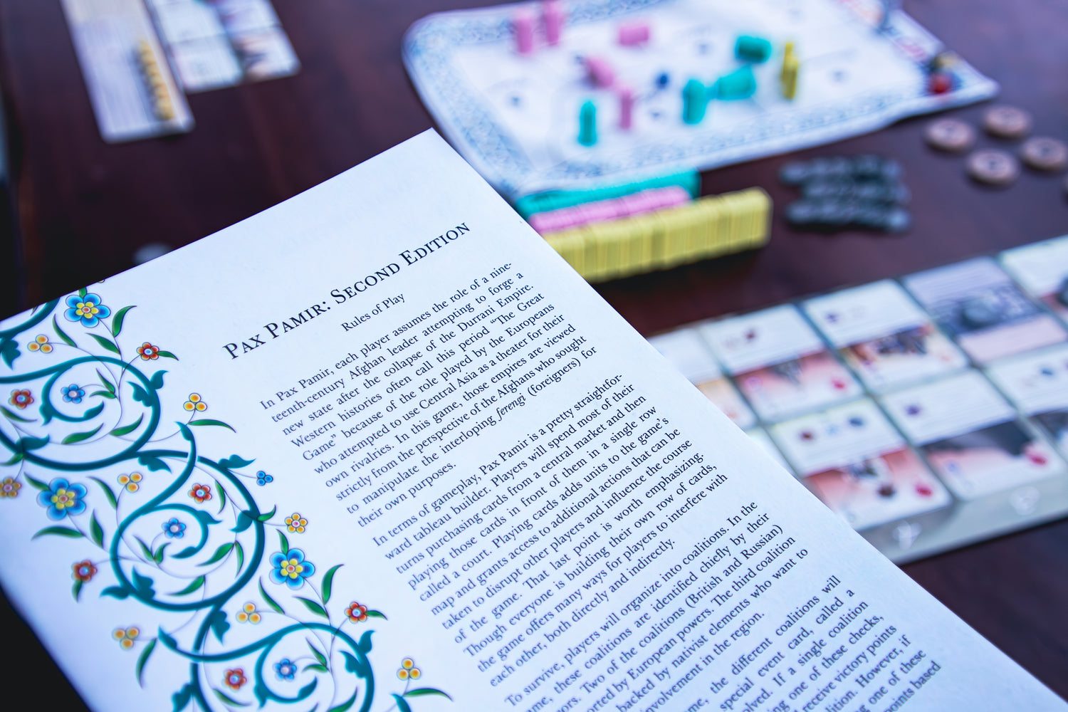 The physical rulebook of Pax Pamir: Second Edition with the game setup in the background.